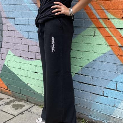 Person wearing black pants with a logo against a colorful mural.
