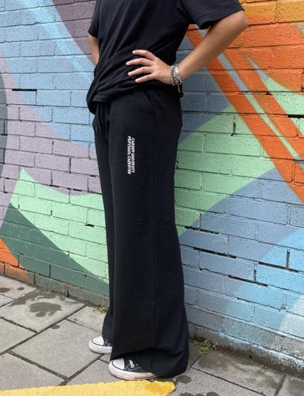 Person wearing black pants with a logo against a colorful mural.