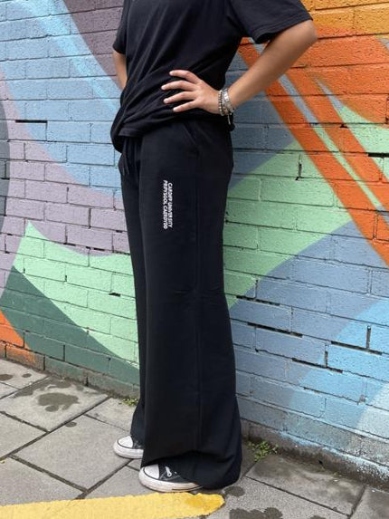 Person wearing black pants with a logo against a colorful mural.